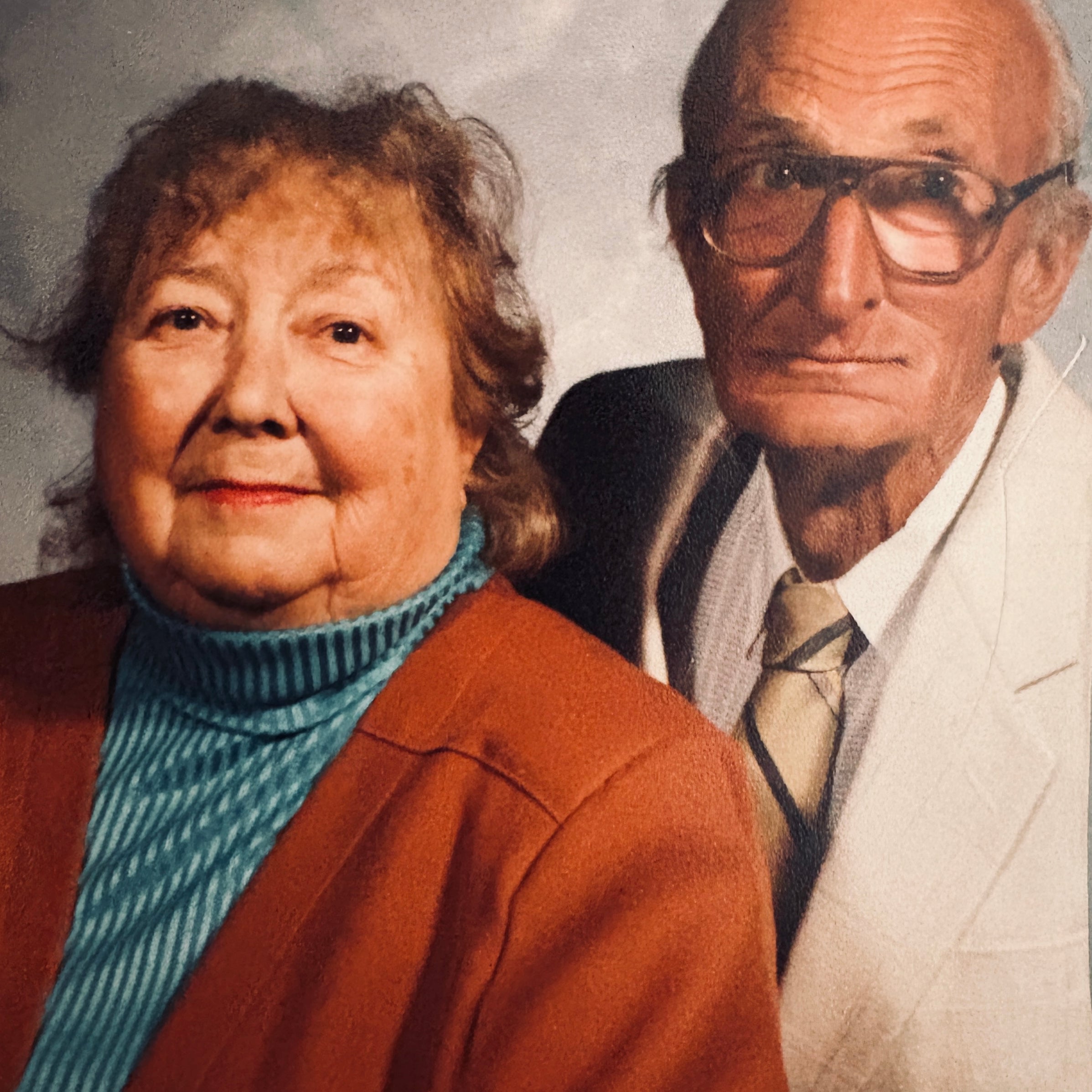 Two elderly people standing side by side against a plain background