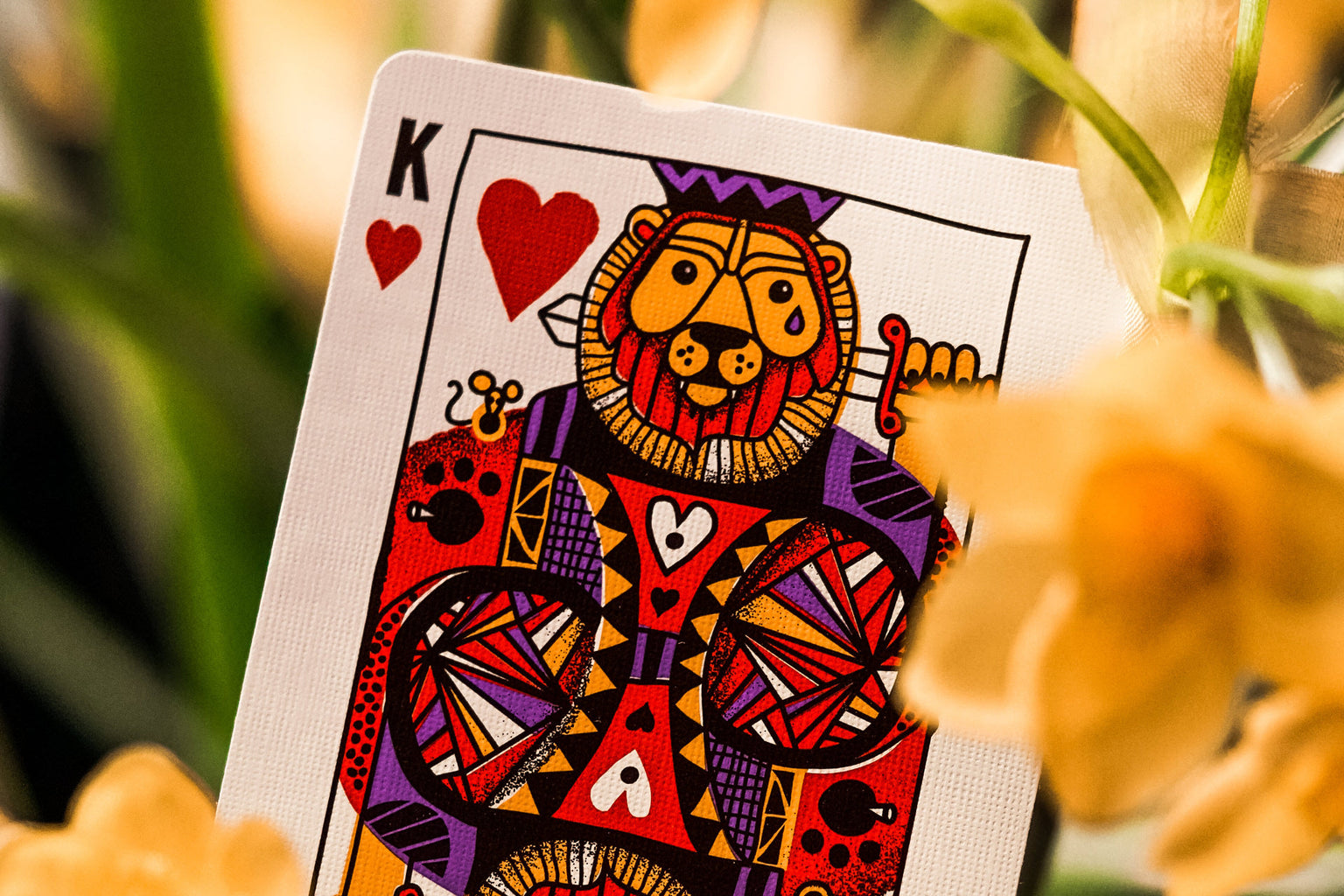 Card with a colorful king of hearts as a lion design, surrounded by flowers.