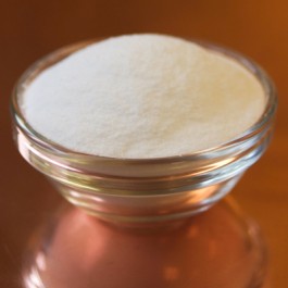 Small glass container with a white sugar on a wooden surface