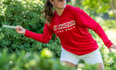Person in a red Innova Disc Golf shirt playing disc golf in a park.
