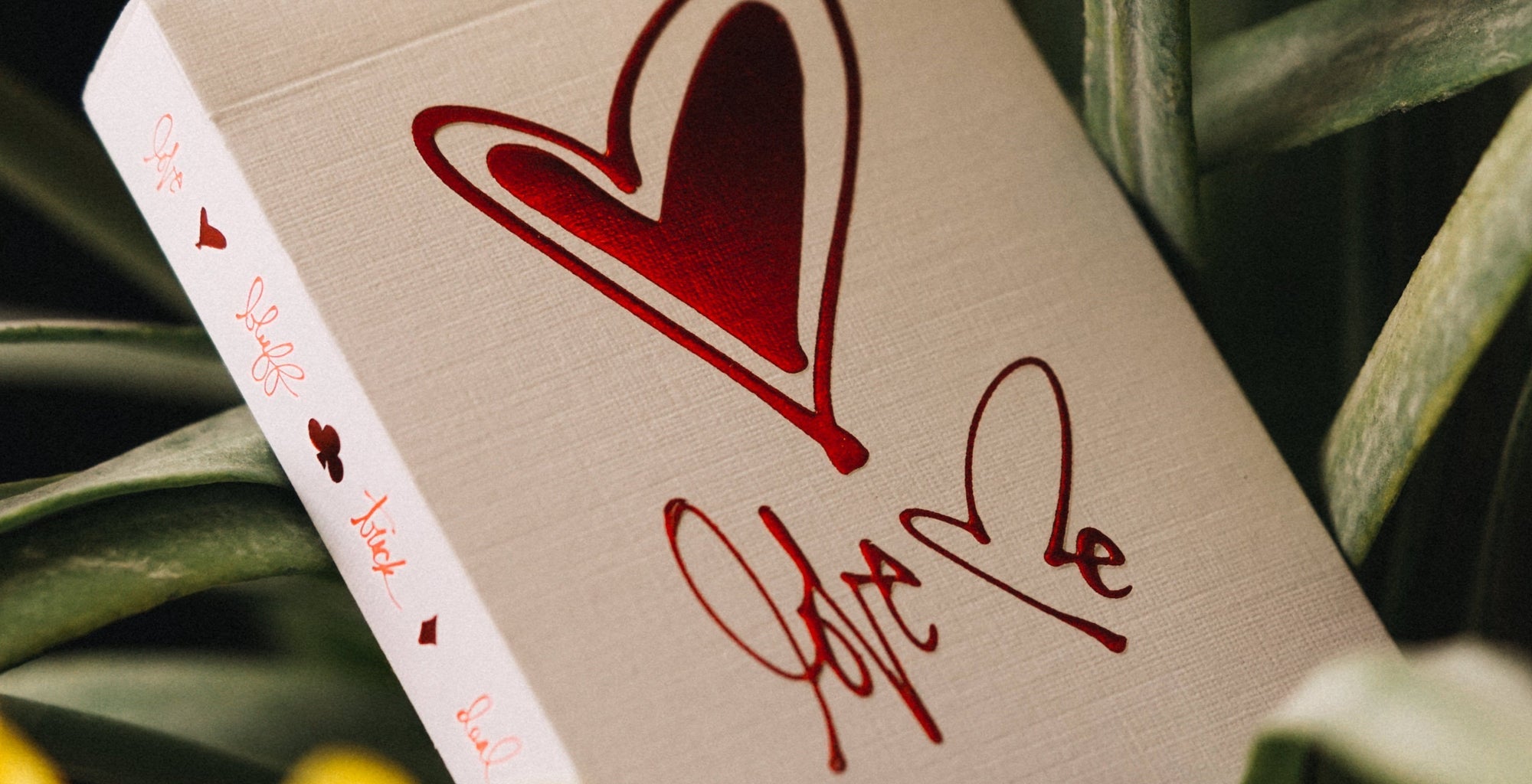 Card with red heart and 'Love' text on a beige background, surrounded by green leaves.