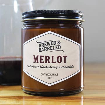 Candle jar labeled 'Brewed & Barreled Merlot' on a wooden surface.