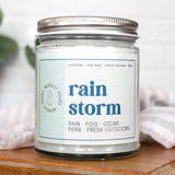 Candle jar labeled 'rain storm' on a wooden surface with a light background