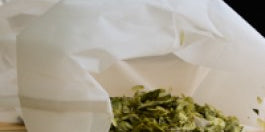Green tea leaves in a white paper bag on a wooden surface