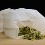 Green tea leaves in a white paper bag on a wooden surface