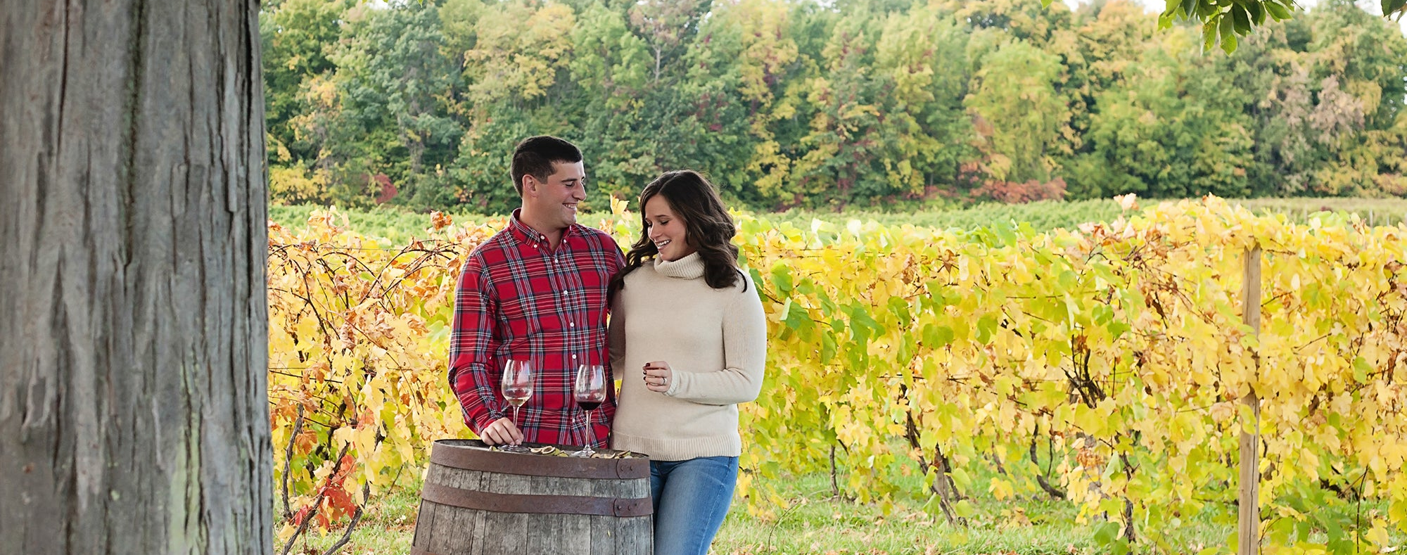Two people standing next to a barrel in a vineyard during autumn.