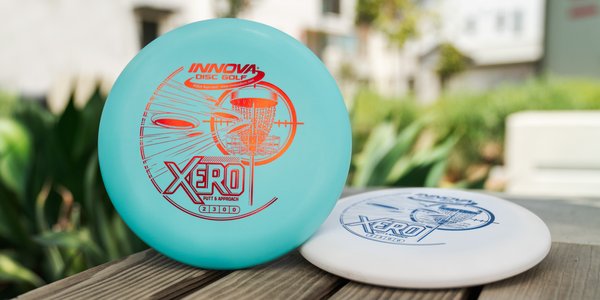 Two disc golf discs on a wooden surface with a blurred outdoor background