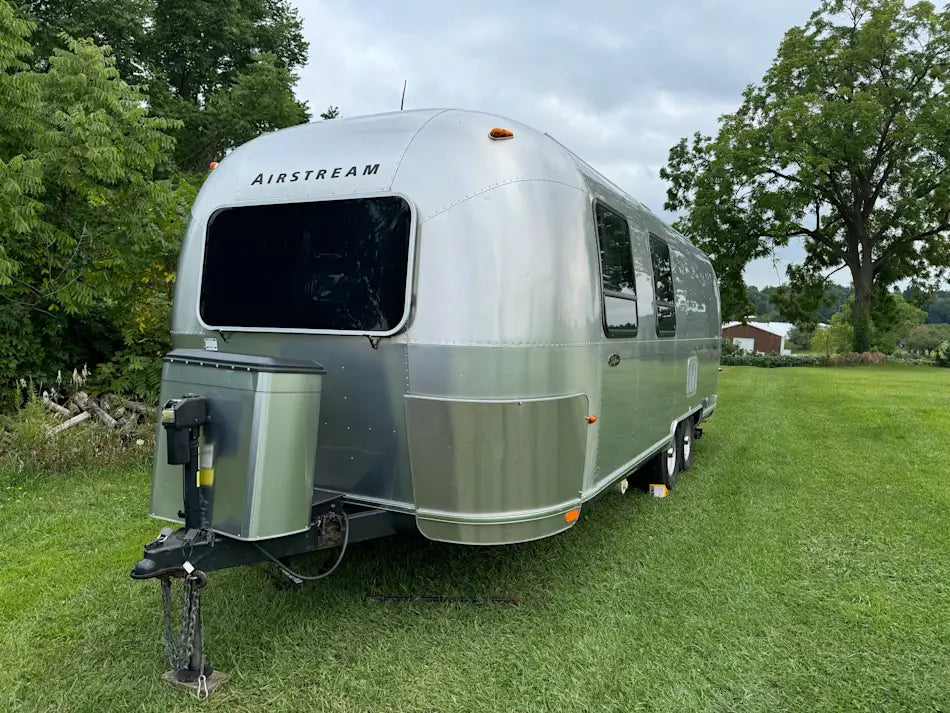 Silver Airstream trailer parked on grass with trees in the background