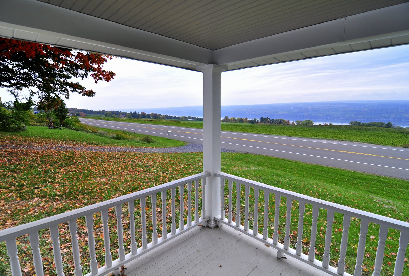 View from a porch overlooking a road and fields with a body of water in the distance.