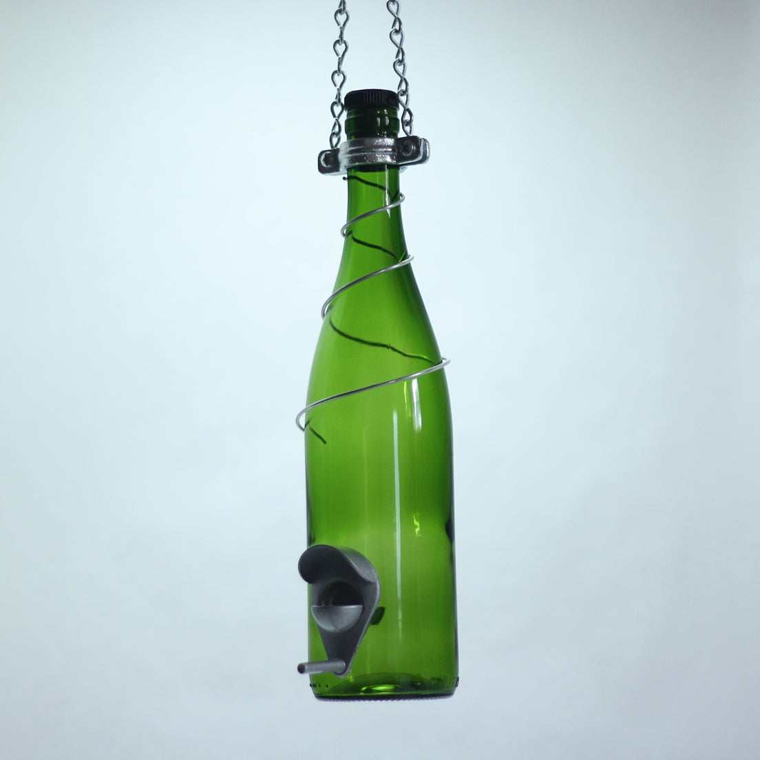 Green glass wine bottle with a metal bird feeder attached on a white background